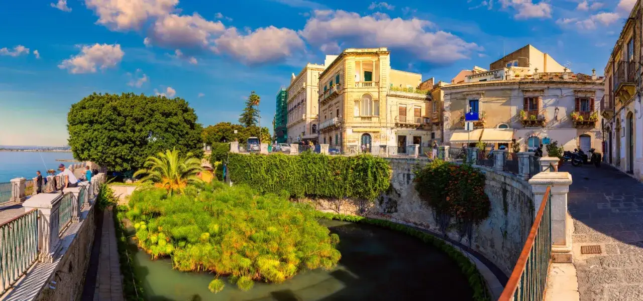 Malowniczy widok na Syrakuzy, Ortigia: zabytkowe budynki, bujna zieleń i kanał z papirusem.