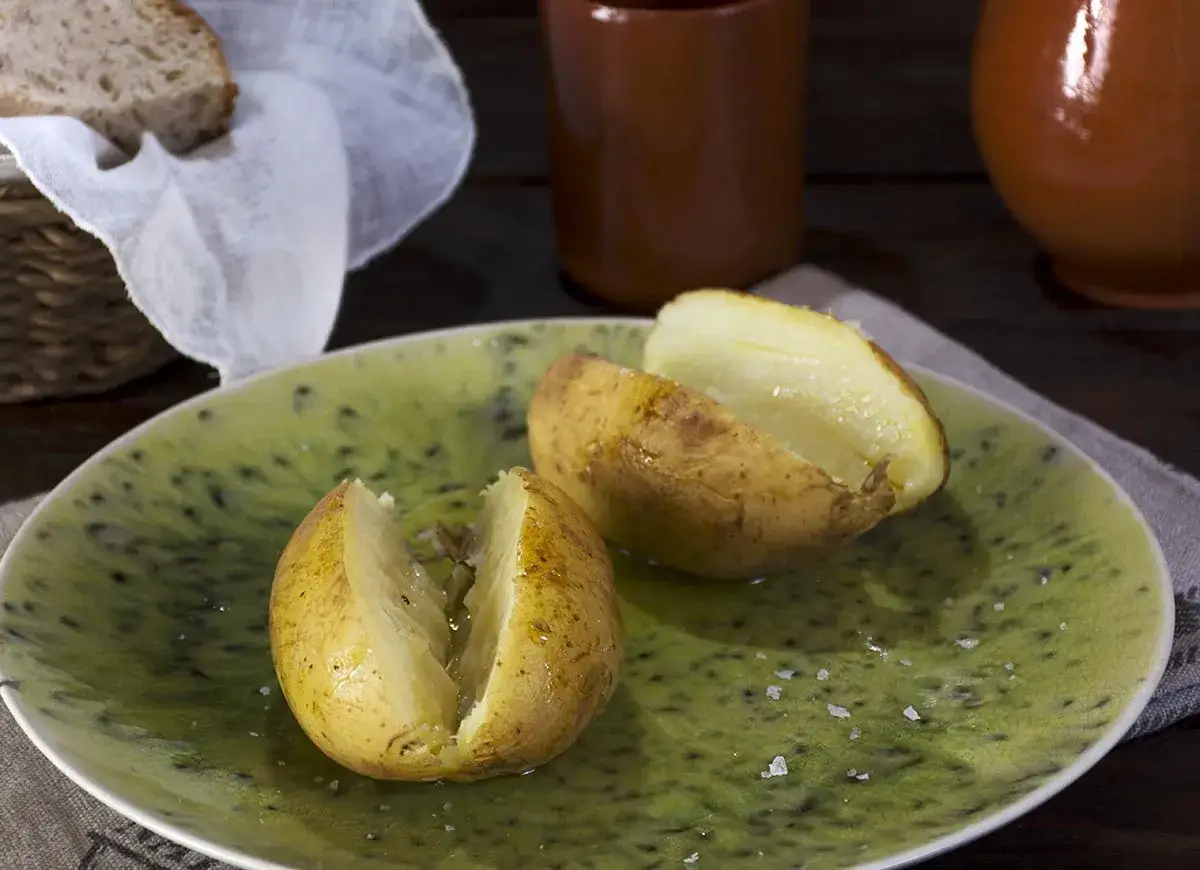 Patatas al microondas, tiernas y doradas, servidas en plato verde con sal.