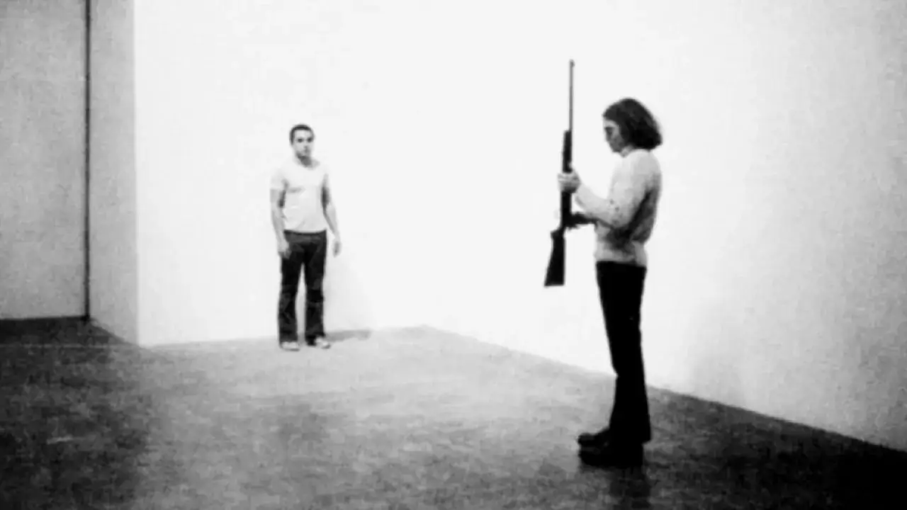 Chris Burden shoot : une femme tient un fusil, un homme se tient à distance. Performance artistique tendue.