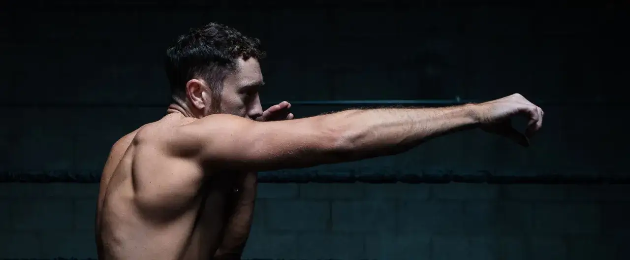 A boxer throws a powerful jab, the most important punch in boxing, in a dimly lit ring.