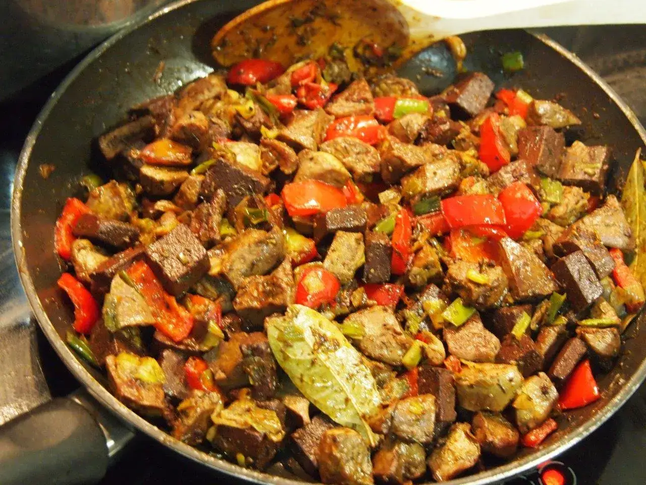 Frito mallorqu&iacute;n en sart&eacute;n, con trozos de carne, pimientos rojos y verdes, y hojas de laurel.