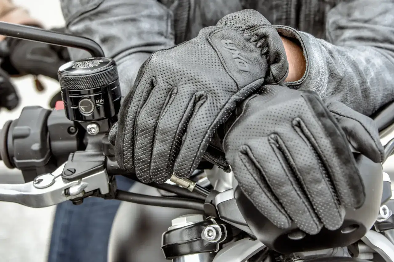 Manos enguantadas en cuero negro sobre el manillar de una moto. Es obligatorio llevar guantes en moto para protegerse.