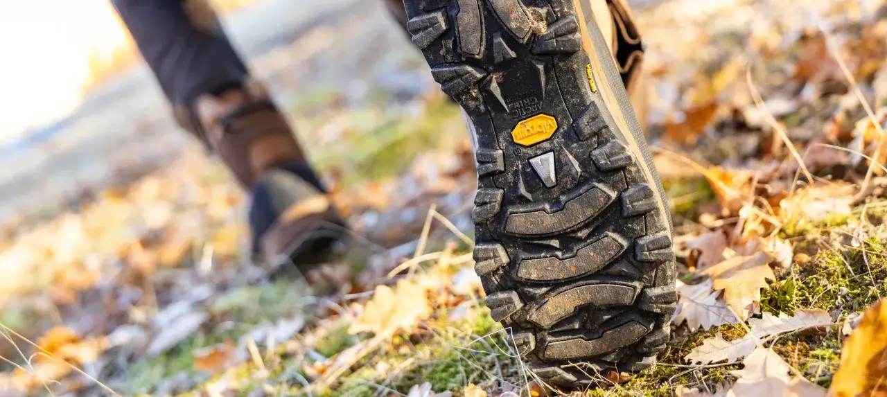 Close-up of a hiking boot sole on a forest floor. Do boots shrink over time? This boot's Vibram sole shows wear, but no signs of shrinking.