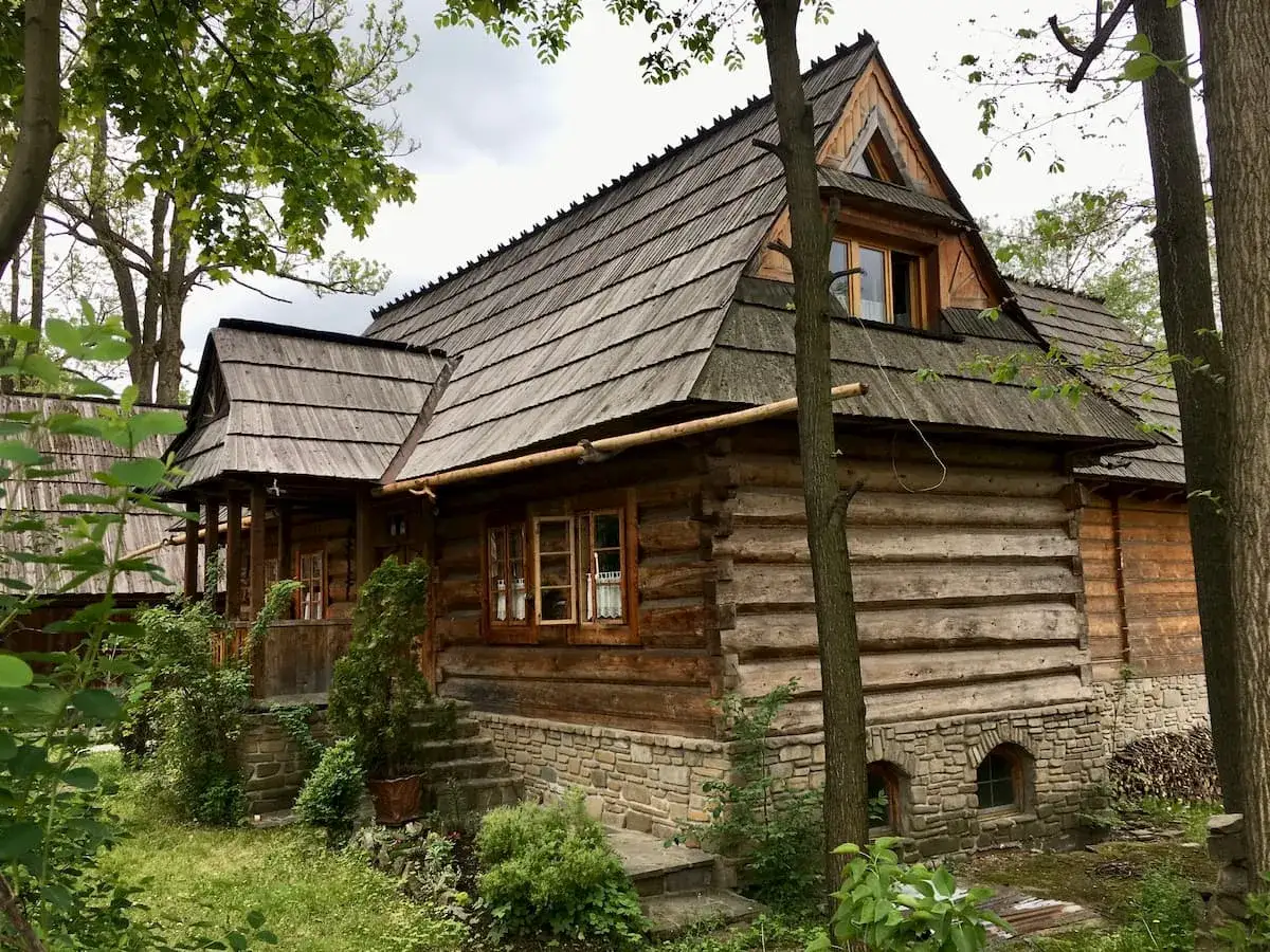 Drewniana chata z kamiennym fundamentem, kryta gontem, otoczona zielenią. Ulica Kościeliska w Zakopanem zachwyca tradycyjną architekturą.