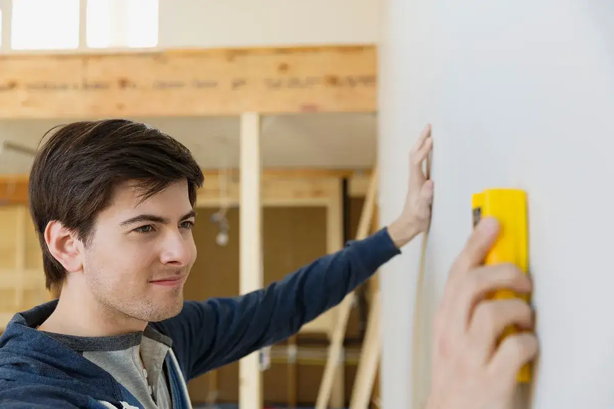Man uses a yellow stud finder on a wall, learning how to use a stud finder for home improvement.