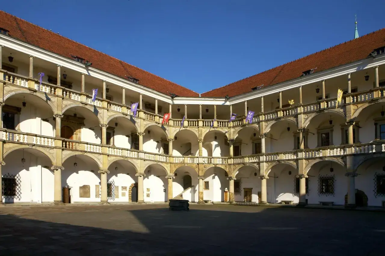Dziedziniec zamkowy z arkadowymi krużgankami, ozdobiony flagami. Wspaniałe **brzeg atrakcje** dla miłośników historii i architektury.