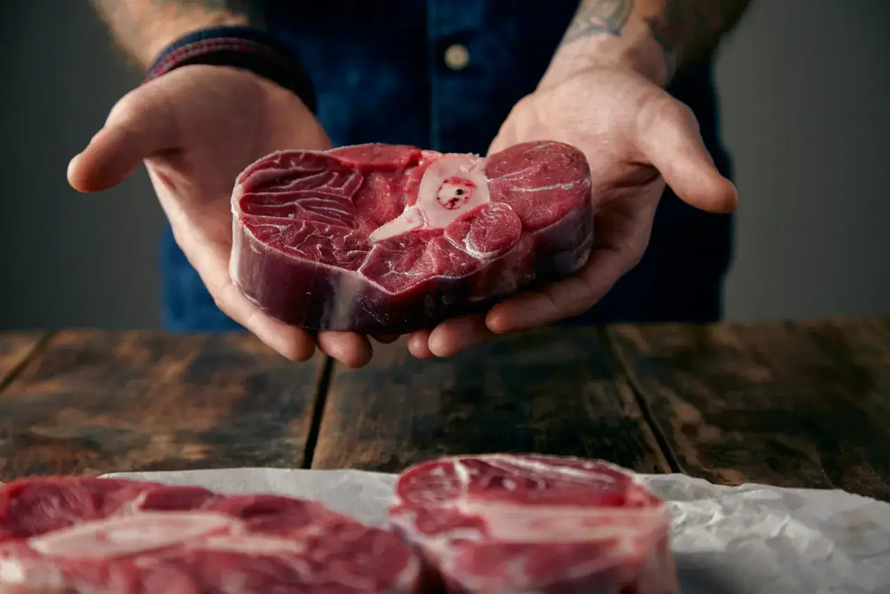 Manos sostienen un corte de carne con hueso, mostrando la calidad de la carne de la finca.