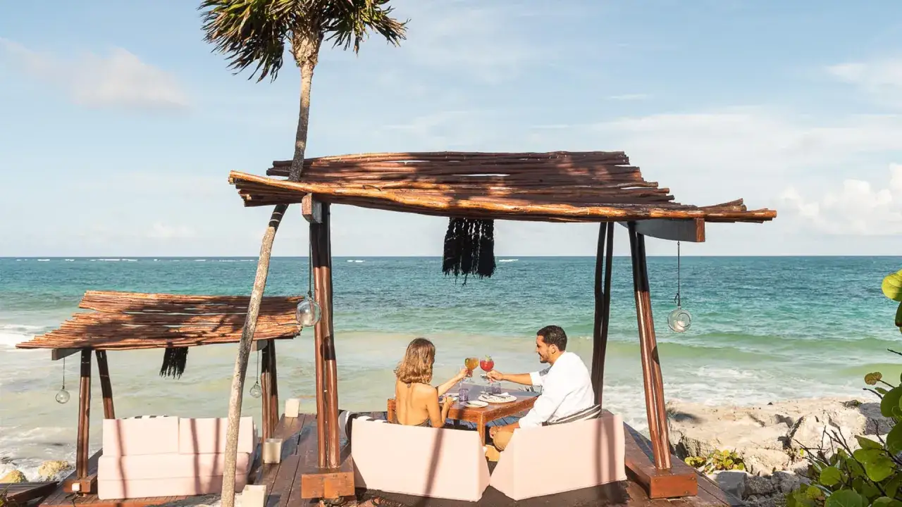 Ein Paar feiert Silvester am warmen Strand. Sie sto&szlig;en mit Cocktails an, w&auml;hrend die Wellen rauschen.