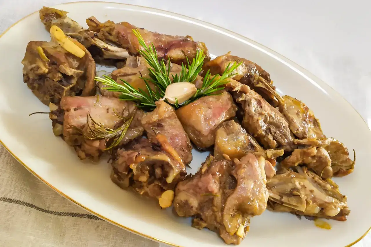 Succulento agnello gratinato al forno, profumato al rosmarino e aglio, servito su un piatto bianco.