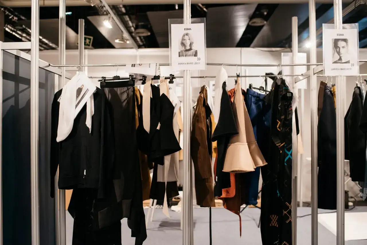 Detrás de escena: ropa de desfile colgada, con fotos de modelos y números. Un vistazo a cómo ser modelo.