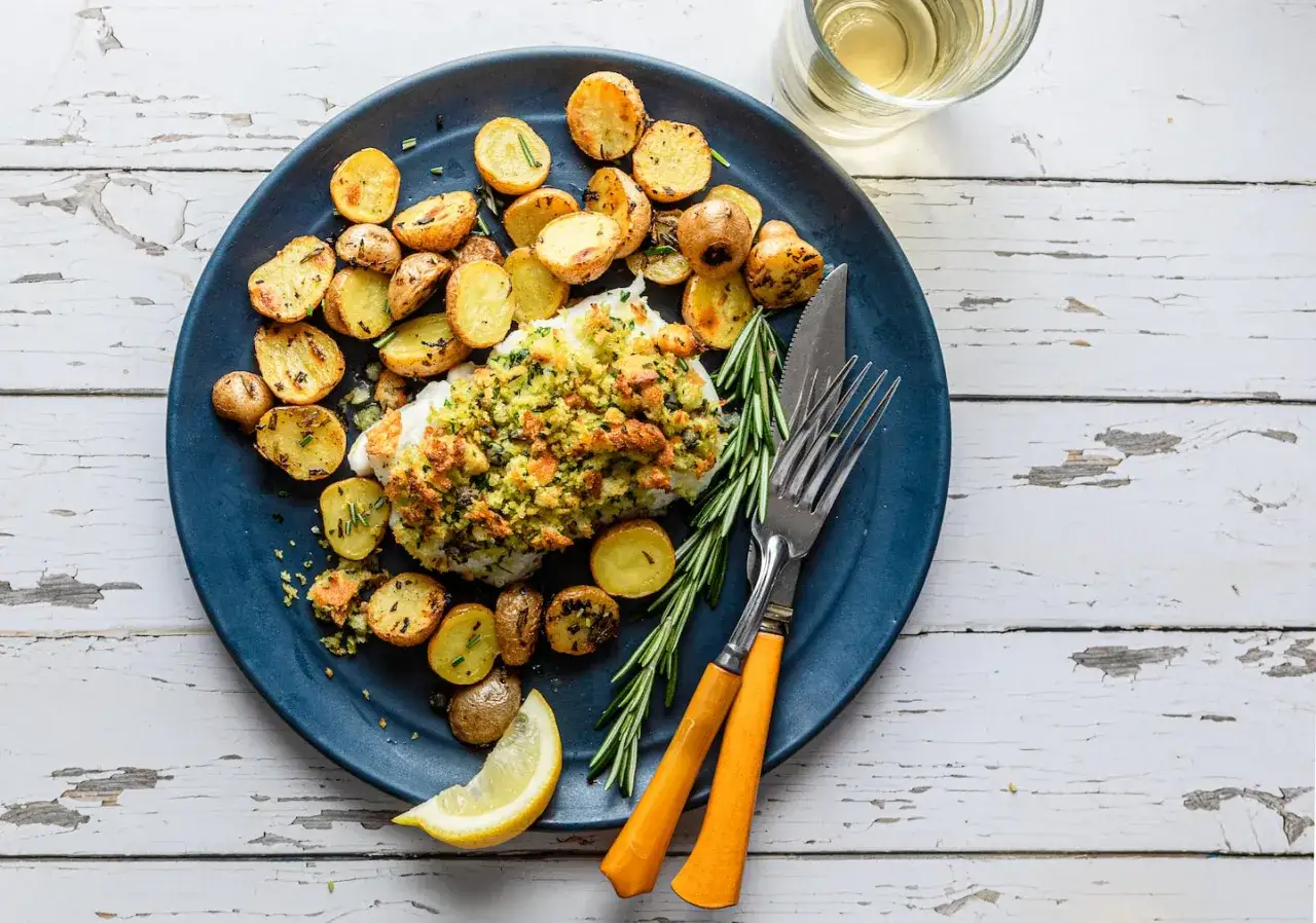 En härlig tallrik med **torsk i ugn**, toppad med krispigt ströbröd och örter, serverad med ugnsrostade potatisar och en citronklyfta.