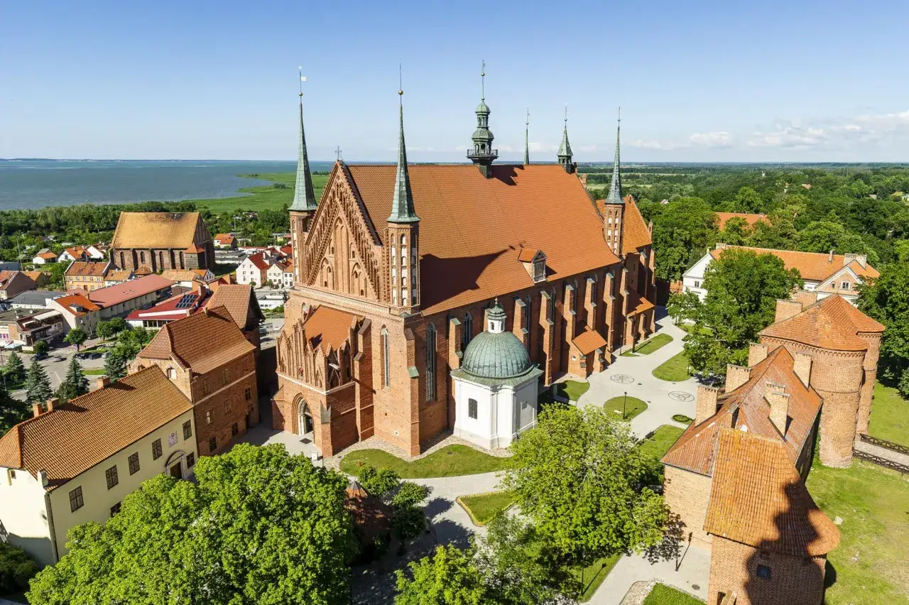 Zamek Frombork z katedrą i wieżami obronnymi, otoczony zielenią i wodą.