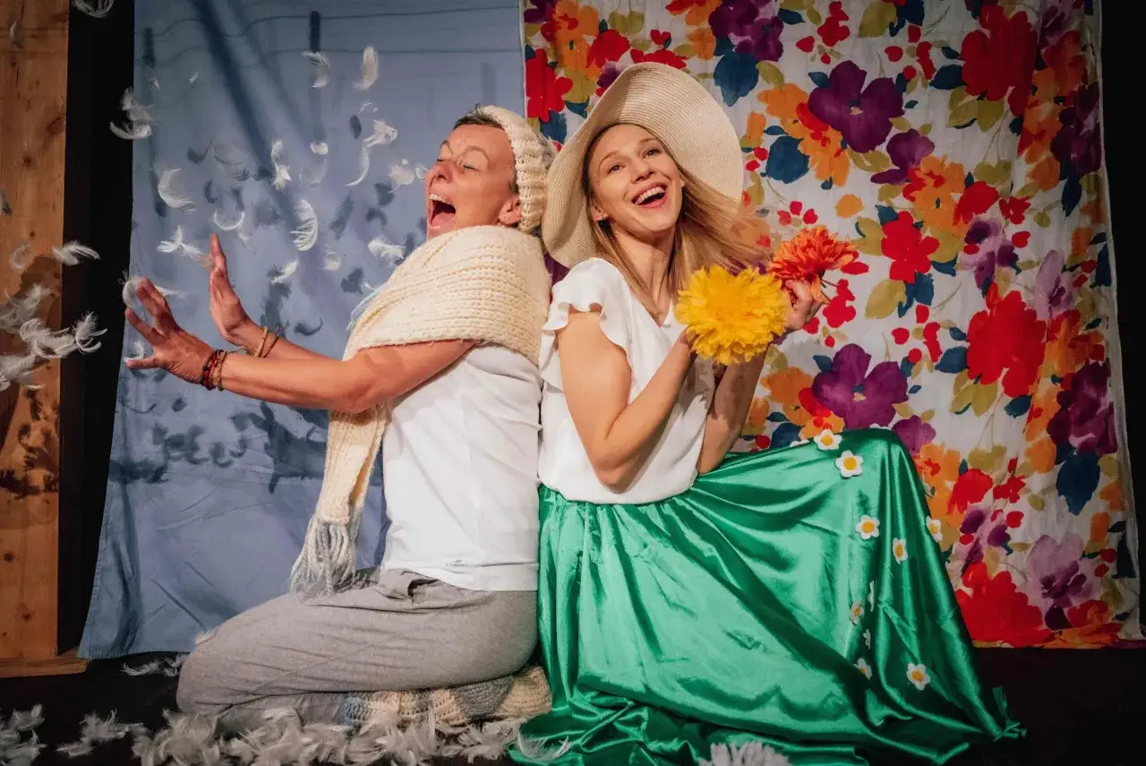 Dwie aktorki w piórach i kwiatach, zapraszają na wesołe przedstawienia teatralne dla dzieci w Warszawie.