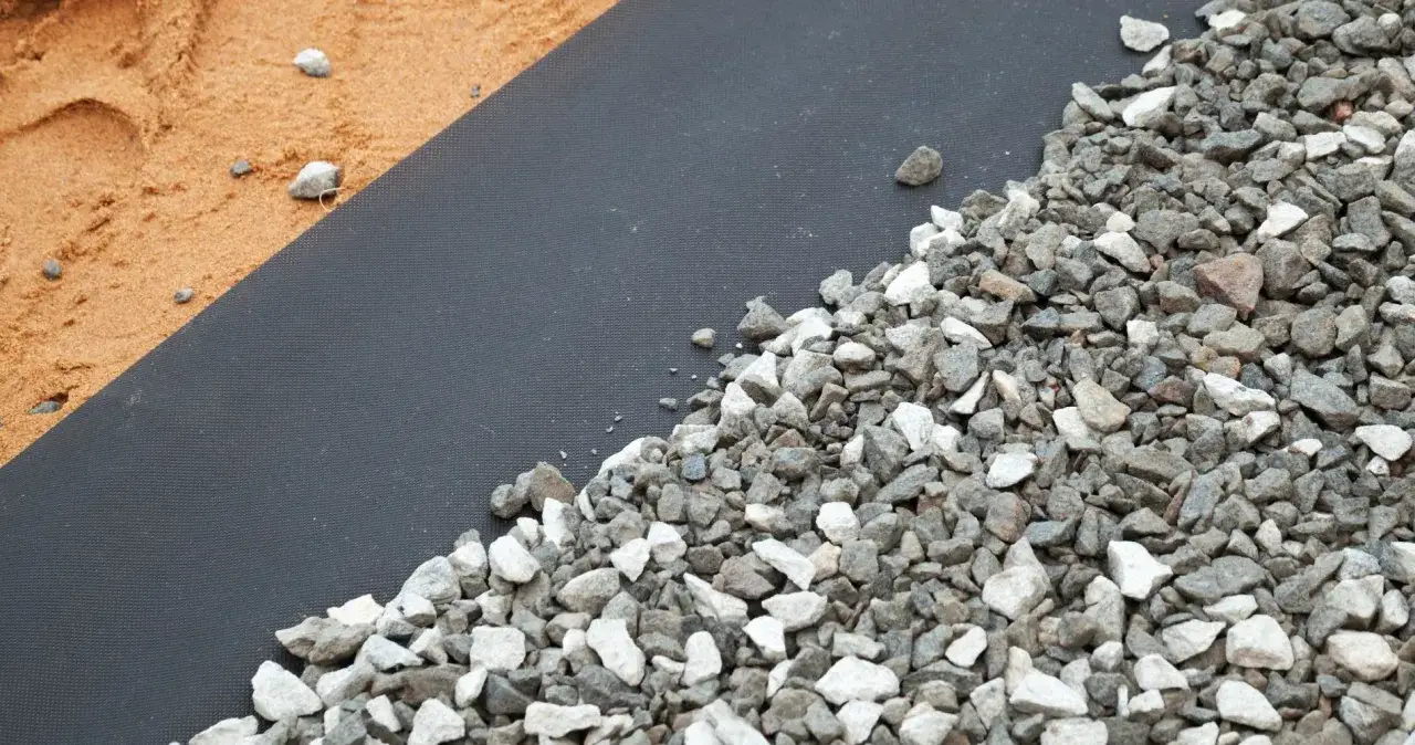 Gravel et sable sur un géotextile noir. Aide à choisir quel geotextile choisir pour vos projets extérieurs.