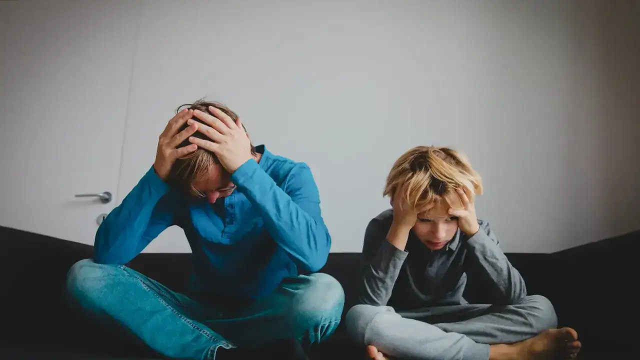 Un padre y un ni&ntilde;o asustado se sientan con las manos en la cabeza, ambos visiblemente angustiados.