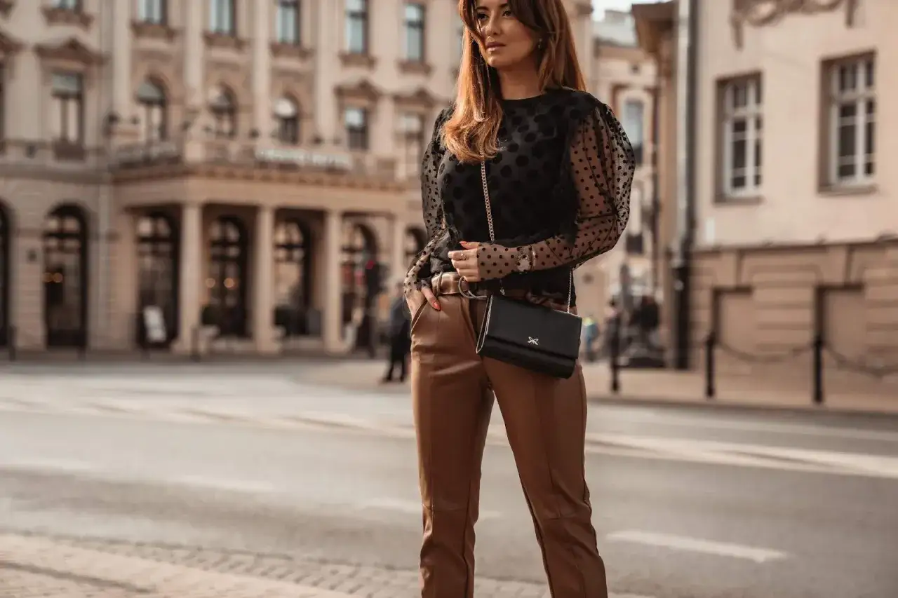 Elegancka stylizacja: czarna bluzka w kropki i brązowe skórzane spodnie. Idealna odpowiedź na pytanie, co ubrać do skórzanych spodni.