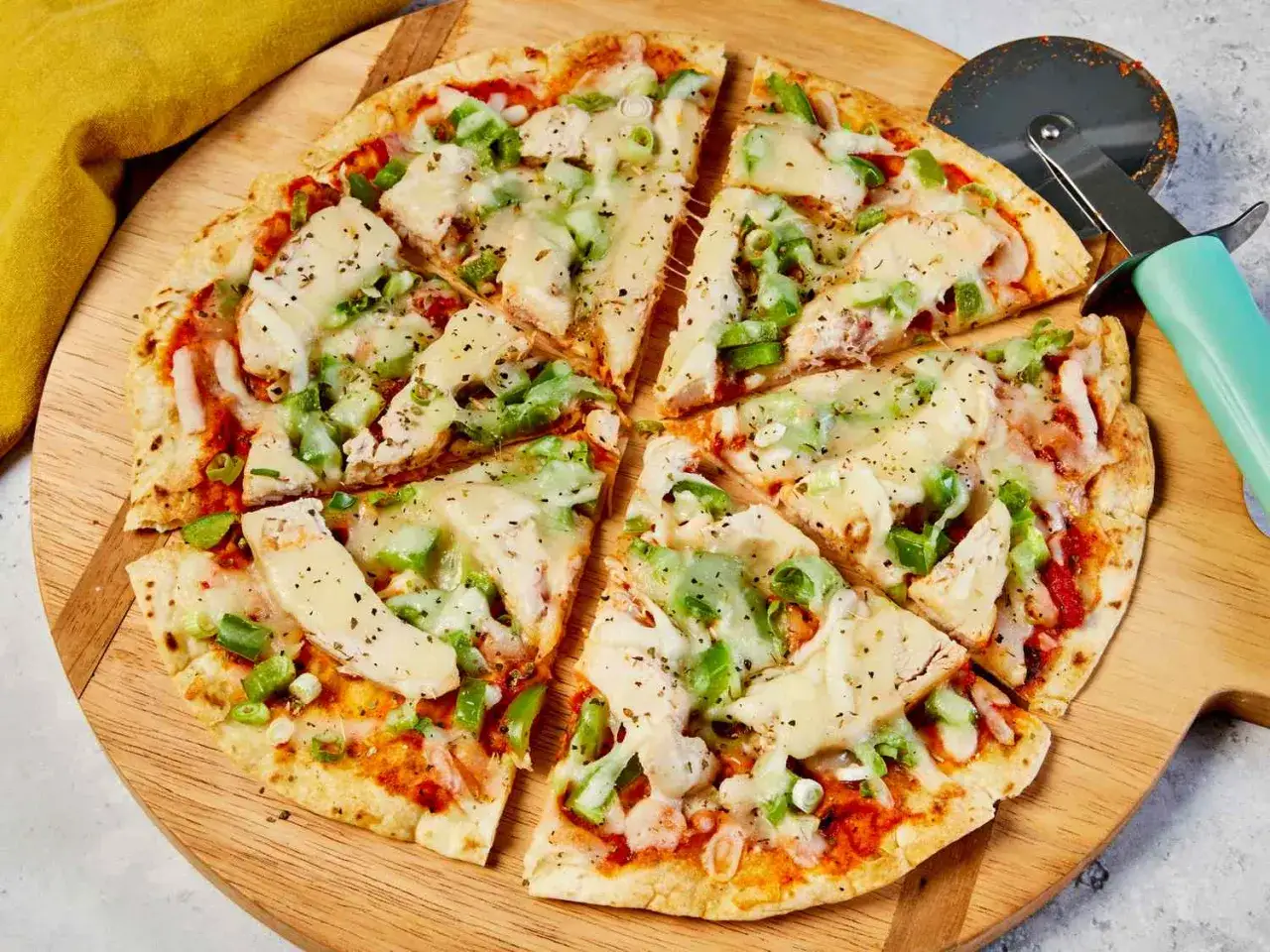 Pyszna pizza na tortilli z kurczakiem i warzywami, pokrojona na kawałki, czeka na talerzu.