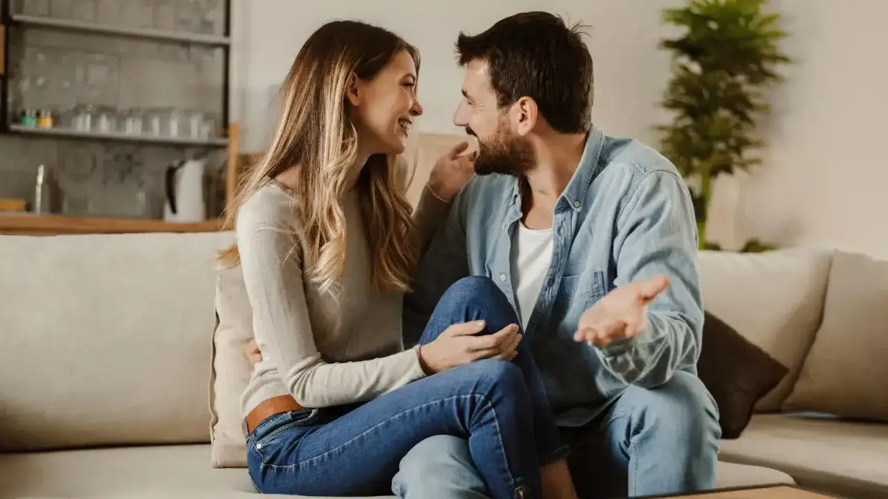 Coppia sorridente seduta sul divano, in un momento di complicit&agrave;. Dimostra che si pu&ograve; stare insieme senza fare l'amore, godendosi la reciproca compagnia.