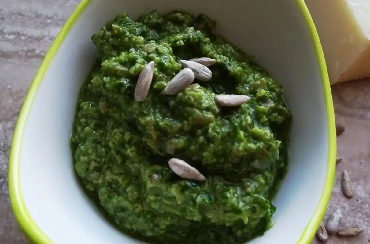 Domowe pesto z bazylii, bogate w smak, ozdobione pestkami słonecznika. Obok kawałek parmezanu.