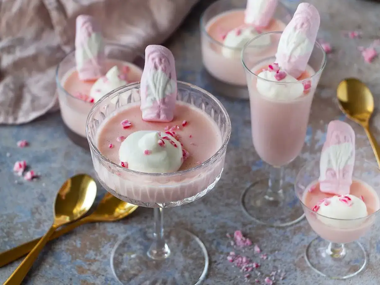 Rosa juleskum pannacotta i glas, toppad med grädde och strössel. En söt och festlig dessert.