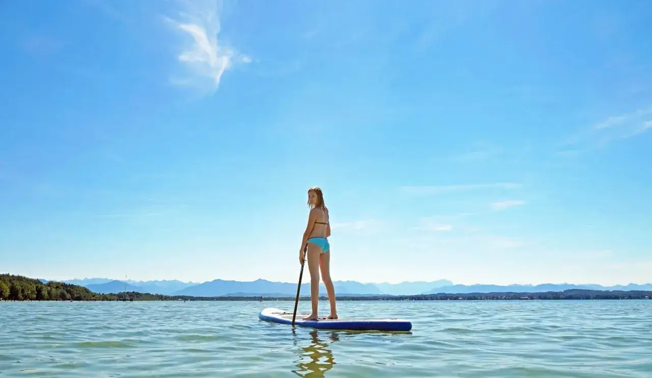 Ein Mädchen genießt eine SUP-Tour in Bayern auf einem ruhigen See vor einer Bergkulisse.
