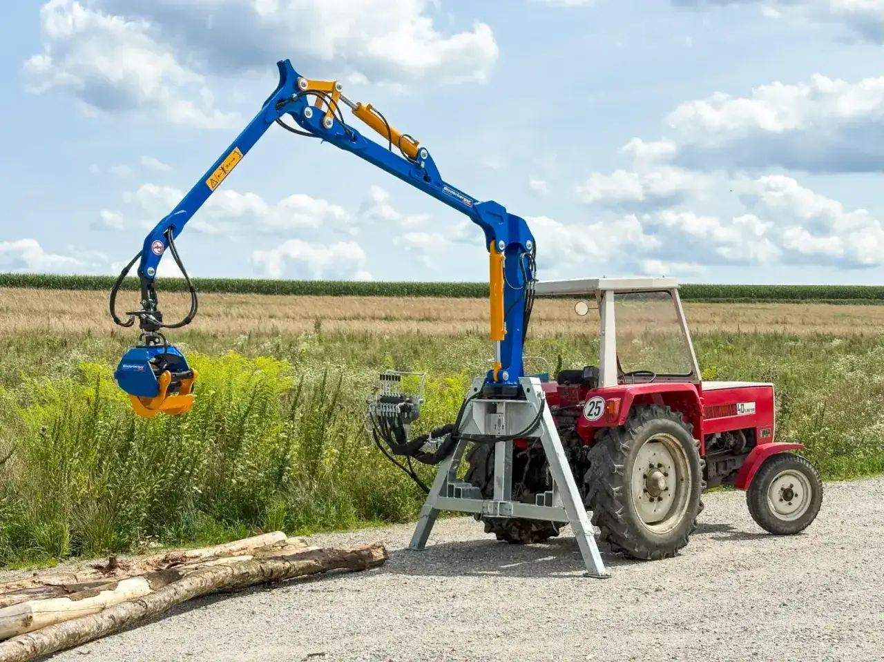 Roter Traktor mit blauem Kran und Greifer, bereit, Holzstämme zu heben.