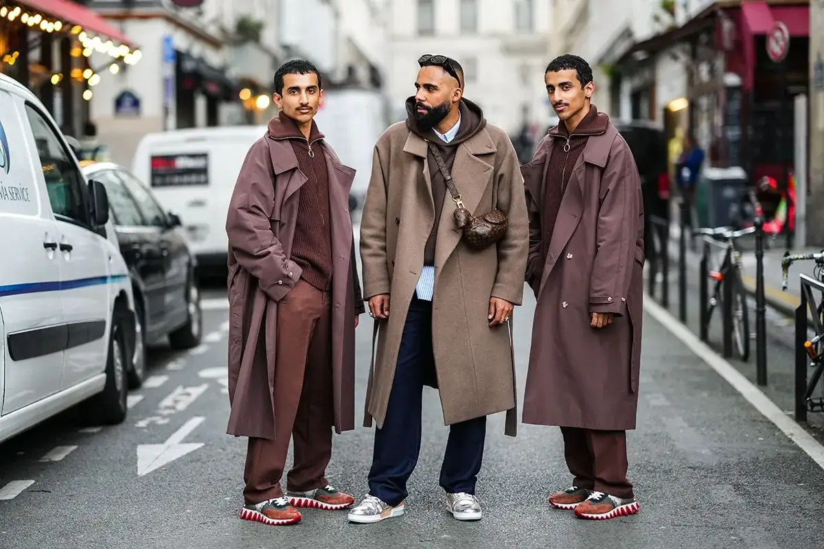 Tre uomini in strada mostrano diversi stili abbigliamento uomo: cappotti lunghi, maglioni a collo alto e pantaloni coordinati, con sneakers audaci.