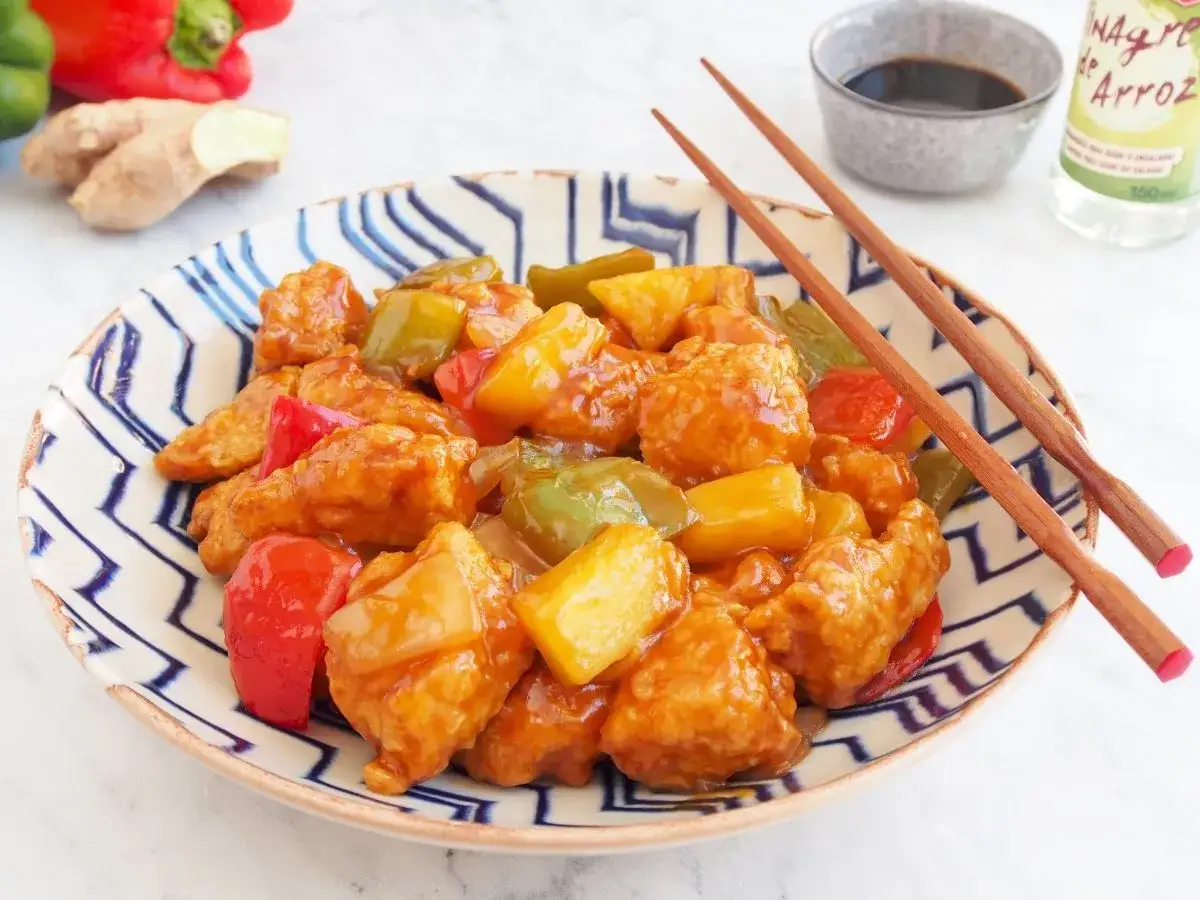 Delicioso cerdo agridulce con trozos de piña y pimientos en una salsa brillante, servido en un plato con palillos.