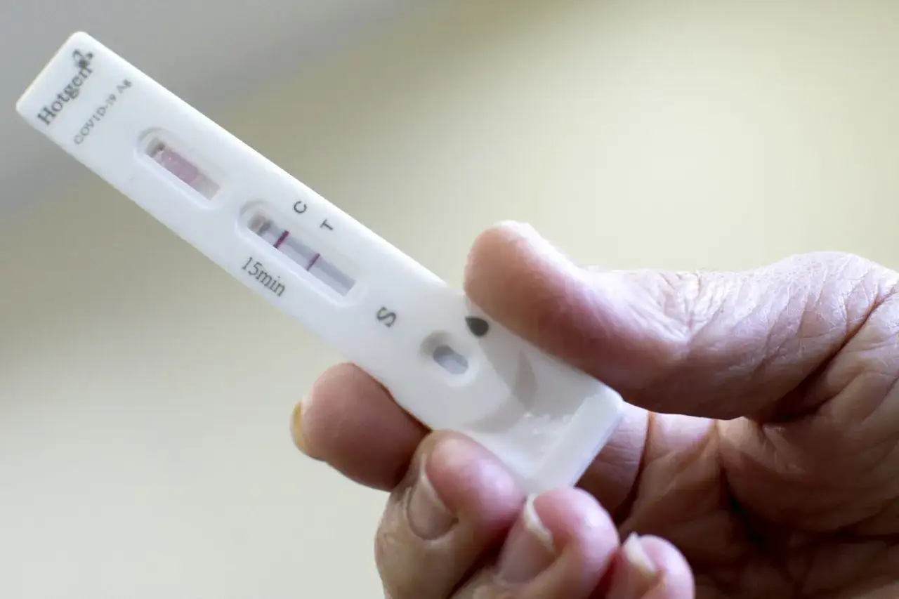 Dłoń trzyma test COVID-19 z dwoma widocznymi paskami, co oznacza pozytywny wynik testu na covid.