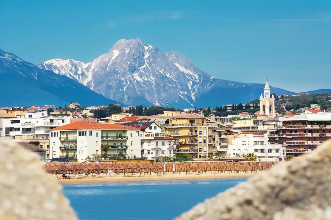 Widok na Pescara, prowincja Pescara, Włochy. W tle ośnieżone góry, przed nimi miasto z kościołem i plaża z parasolami.