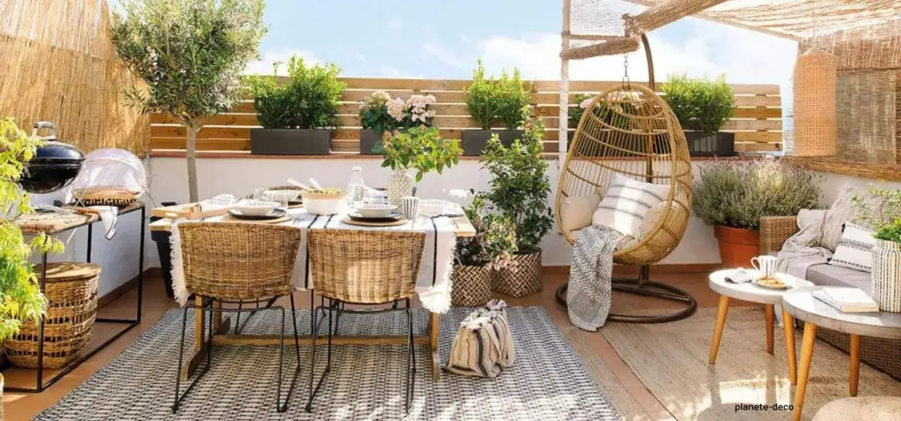 Terrasse am&eacute;nag&eacute;e avec table, chaises en rotin, fauteuil suspendu et plantes. Une belle id&eacute;e jardin sans pelouse pour un espace convivial et fleuri.