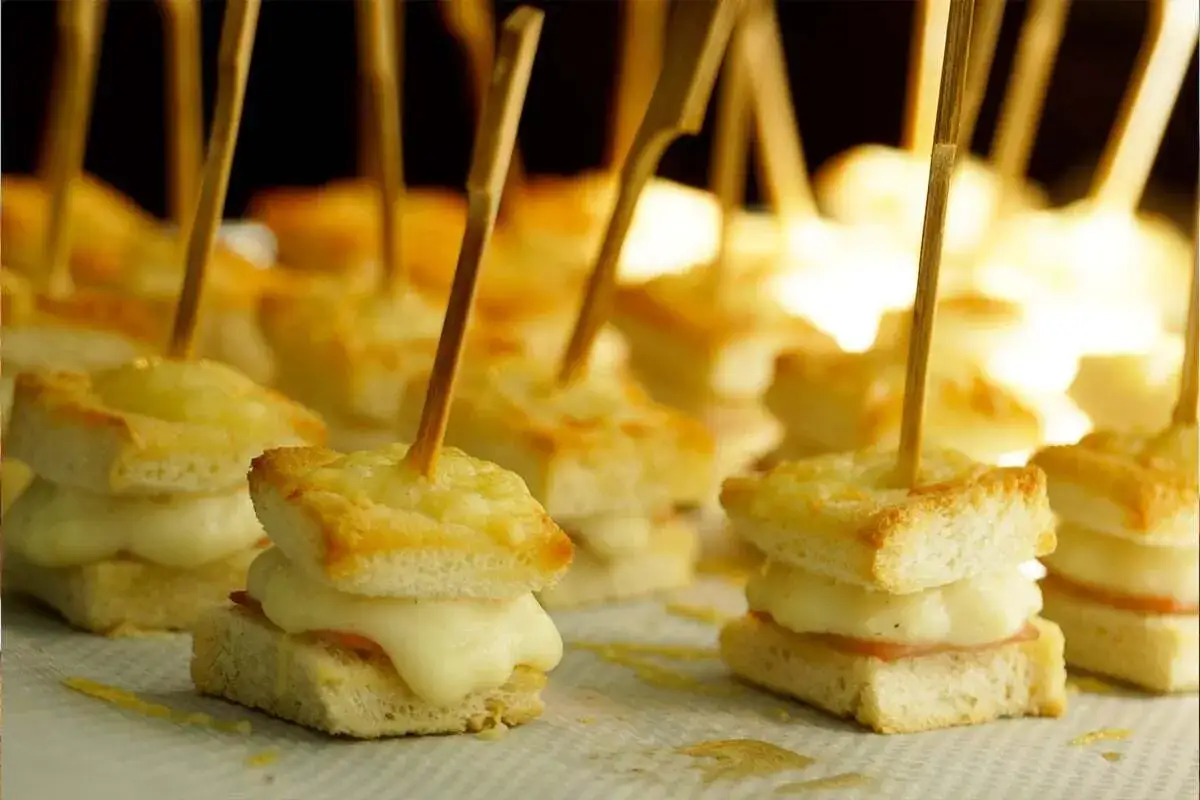 Petits sandwichs gourmands avec du jambon et du fromage fondant, piqués de bâtonnets en bois.