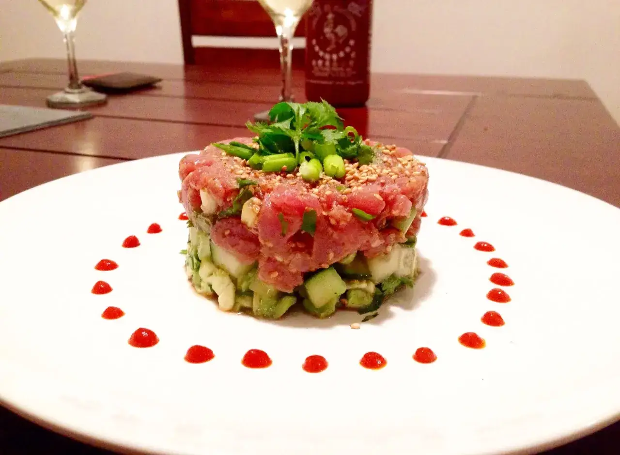 Delicioso tartar de atún fresco con aguacate y pepino, decorado con semillas de sésamo y un toque picante.