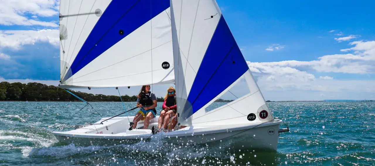 Deux jeunes femmes naviguent sur un voilier RS Venture par une journée ensoleillée.