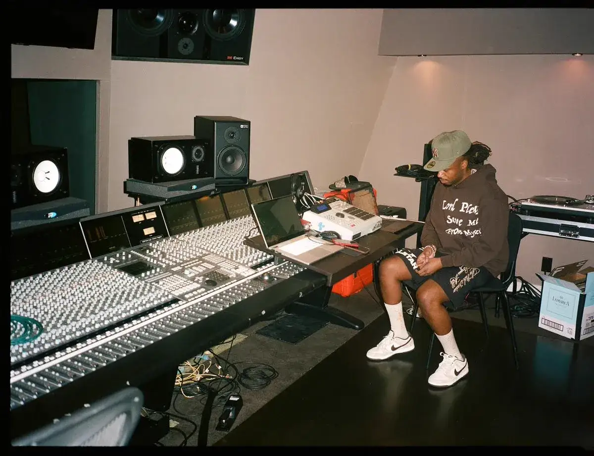 Productor en estudio de grabación, rodeado de equipo, quizás creando la diferencia entre rap y trap.