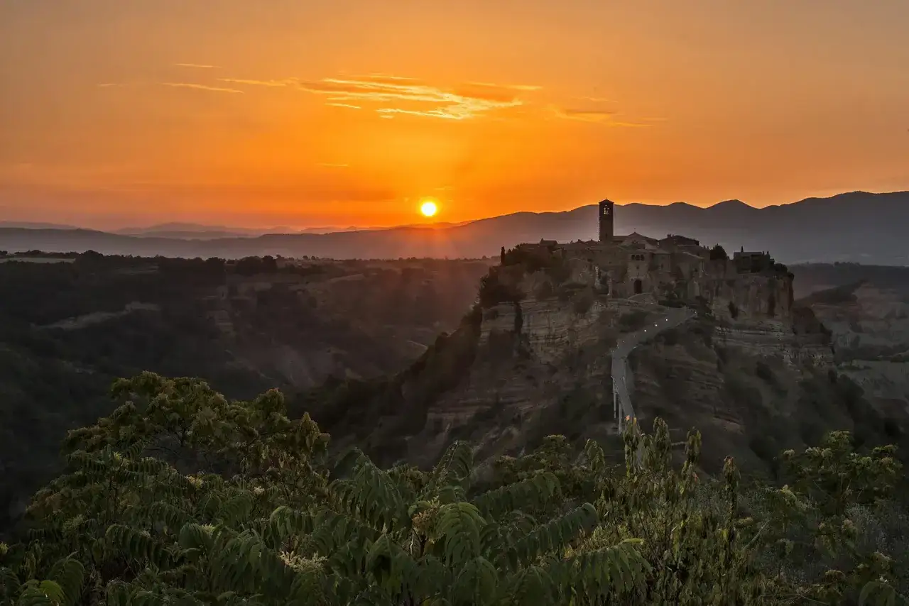 Tramonto infuocato su Civita di Bagnoregio, un borgo arroccato su una rupe, illuminato dalla luce dorata del sole calante.