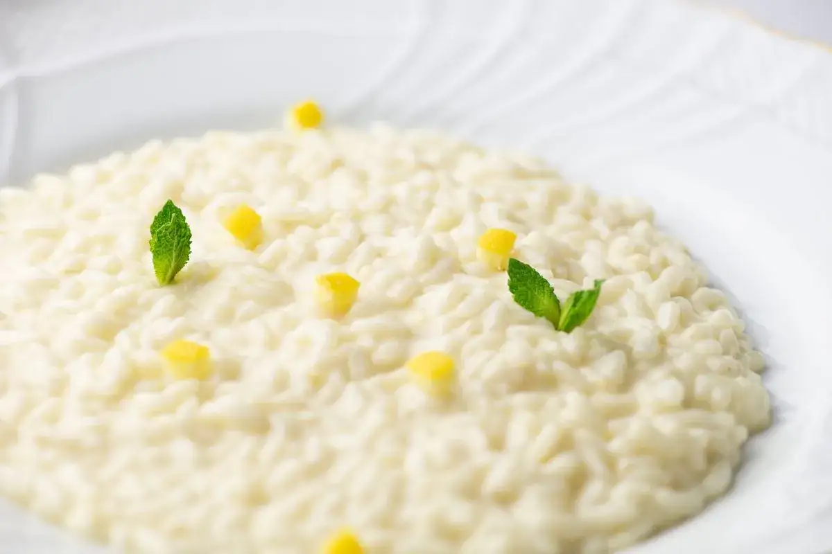 Un cremoso risotto al limone, guarnito con cubetti di scorza di limone e foglioline di menta fresca, su un piatto bianco.