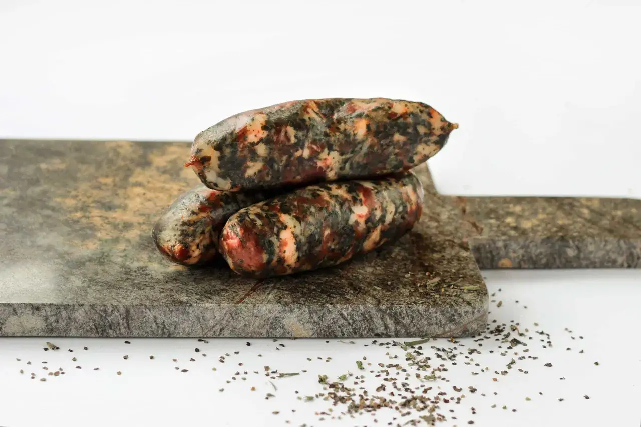 Trois saucisses aux herbes sur une planche de granit, prêtes pour une recette de pormonier.