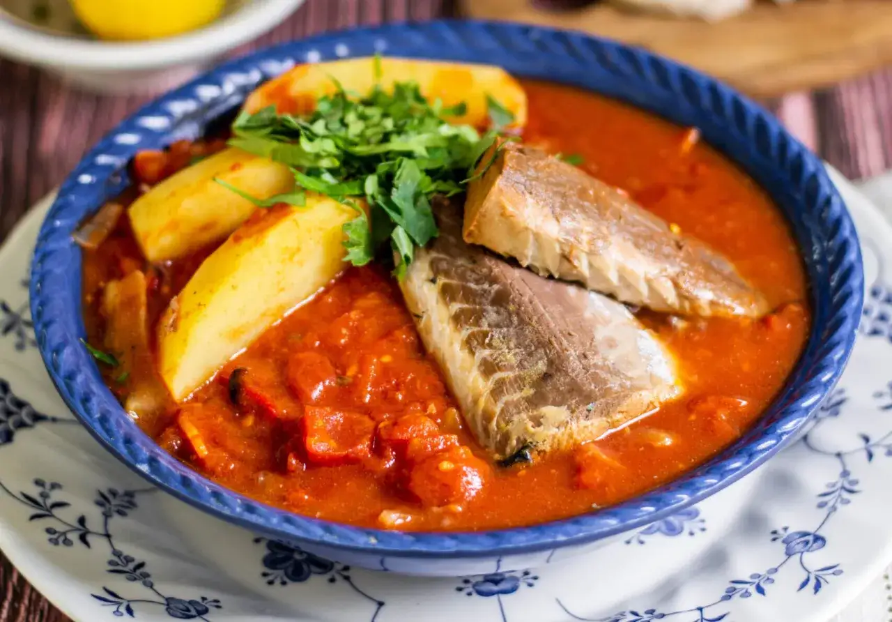 Un sabroso guiso de jurel pescado con patatas y salsa de tomate, adornado con perejil fresco.