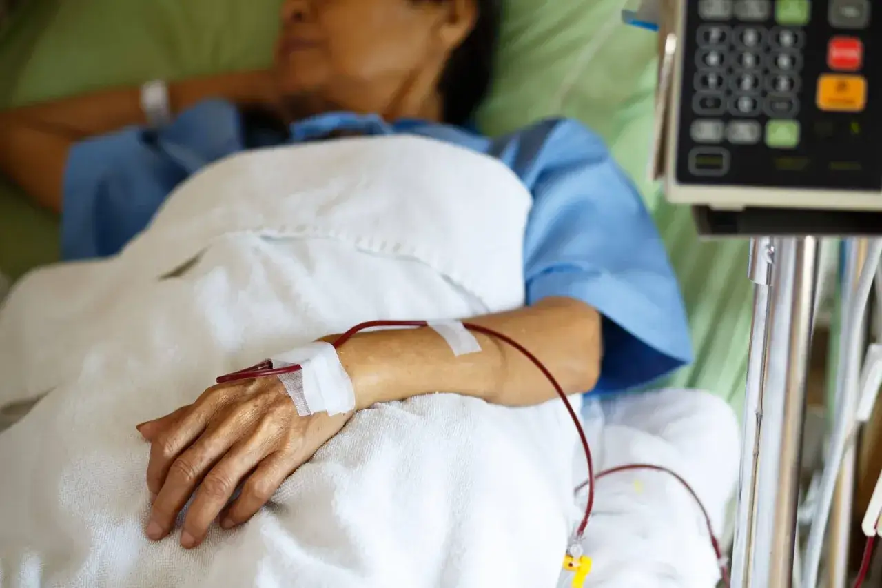 Pacjent podłączony do aparatury medycznej, z czerwoną linią krwi widoczną w żyle. Czy przetaczanie krwi jest bezpieczne? Tak, przy odpowiednich procedurach.