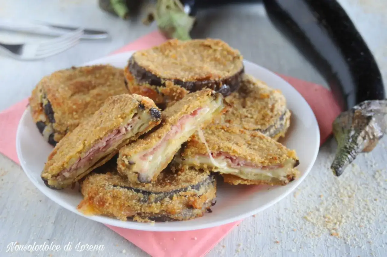 Cordon bleu di melanzane impanati e fritti, ripieni di prosciutto e formaggio filante, serviti su un piatto bianco.