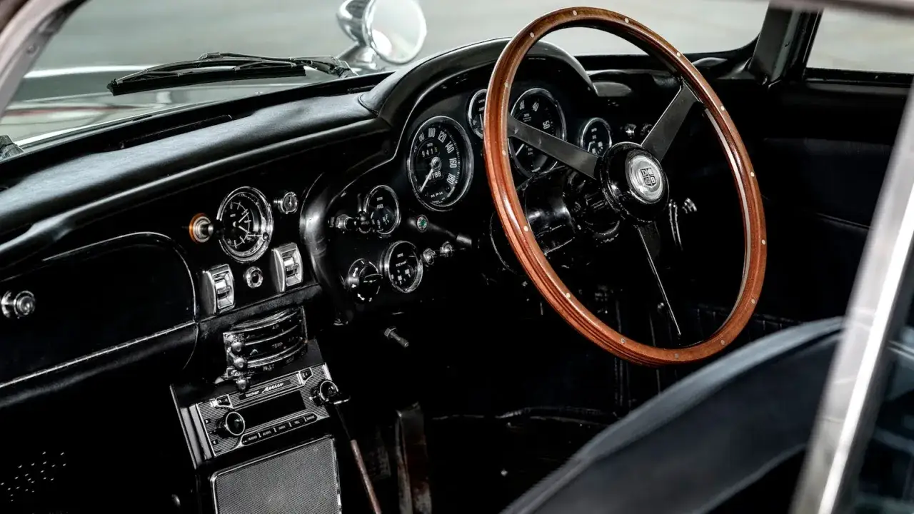 Interi&ouml;r i en Aston Martin DB5 med klassisk tr&auml;-ratt och instrumentpanel.