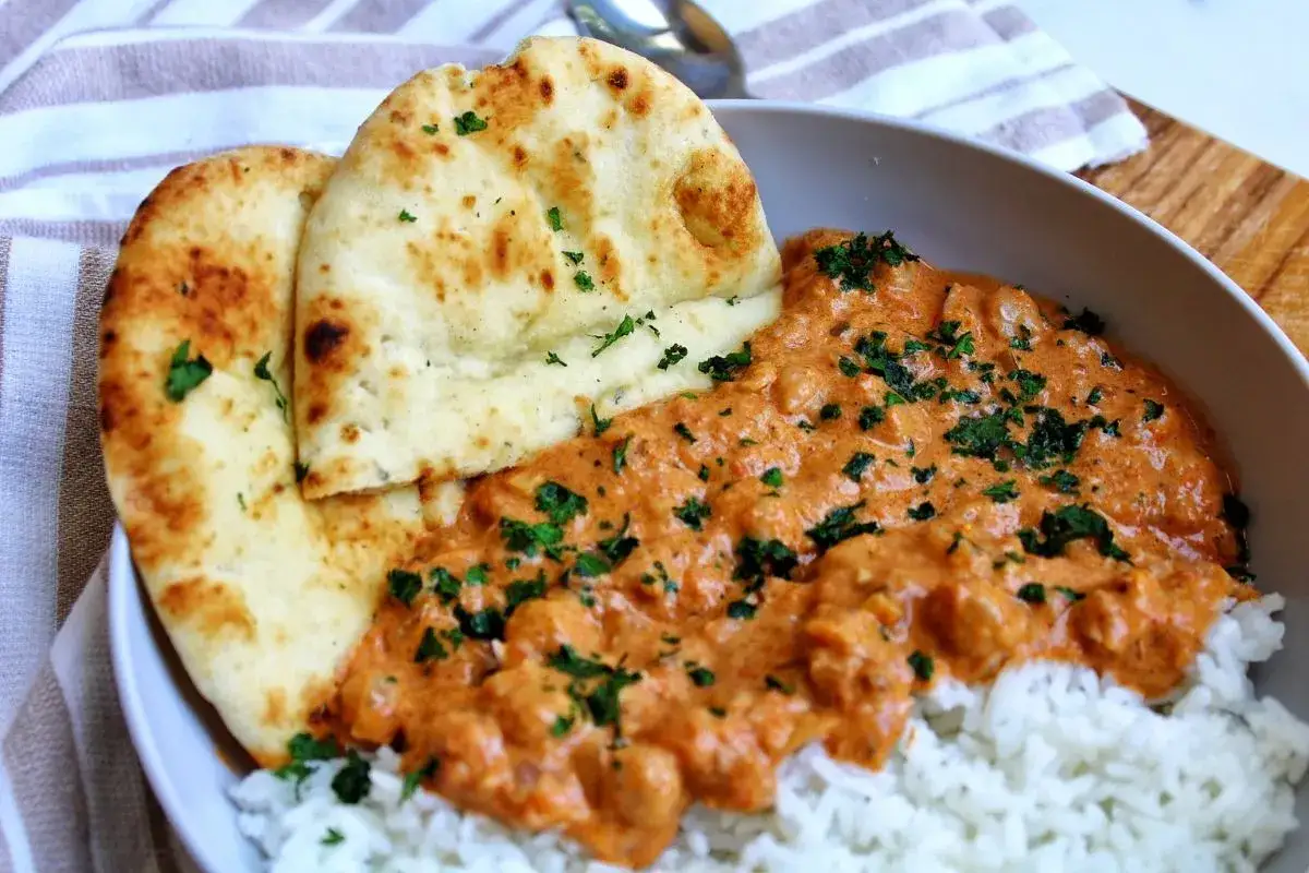 Aksamitne curry z ciecierzycy podane z ryżem i chlebkiem naan, posypane świeżą natką pietruszki.