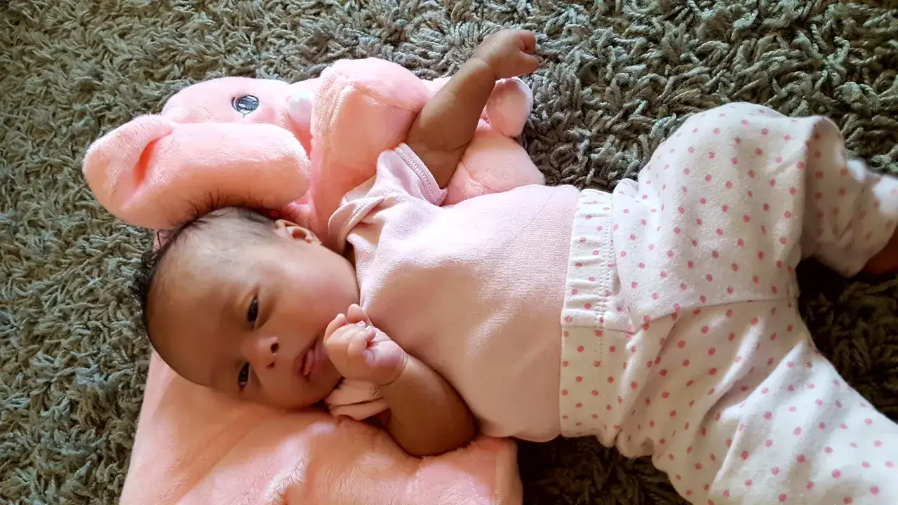 Un neonato con sindrome di Down, vestito di rosa, gioca con un peluche.