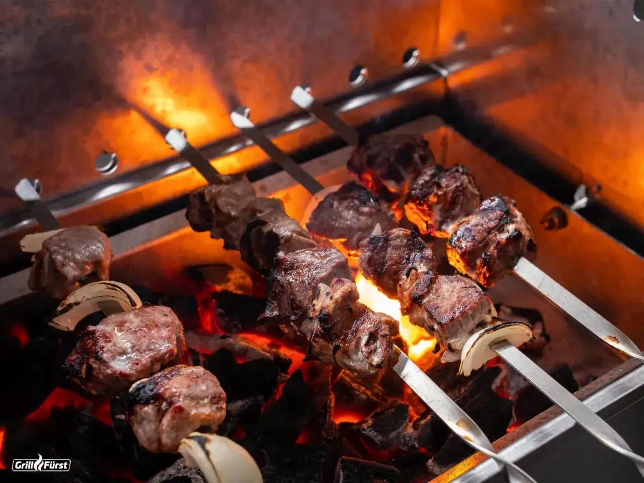 Fleisch zum Grillen ziseliert auf Spie&szlig;en &uuml;ber gl&uuml;hender Kohle, mit Zwiebelst&uuml;cken dazwischen. Die Flammen werfen ein warmes Licht.