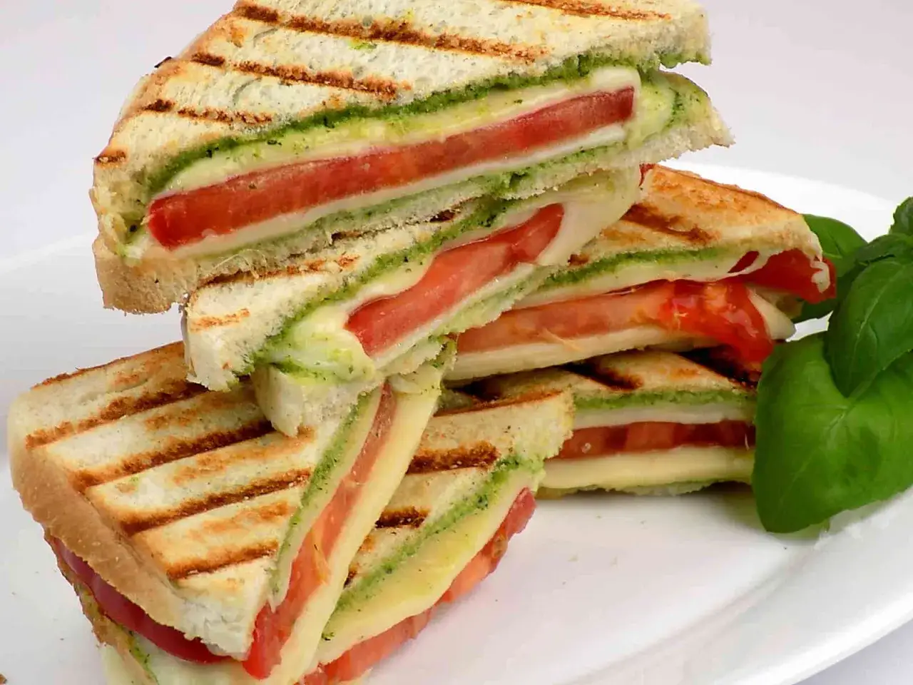 Pyszne kanapki z mozzarellą, pomidorami i zielonym pesto, grillowane na złoto. Idealne na szybki lunch.