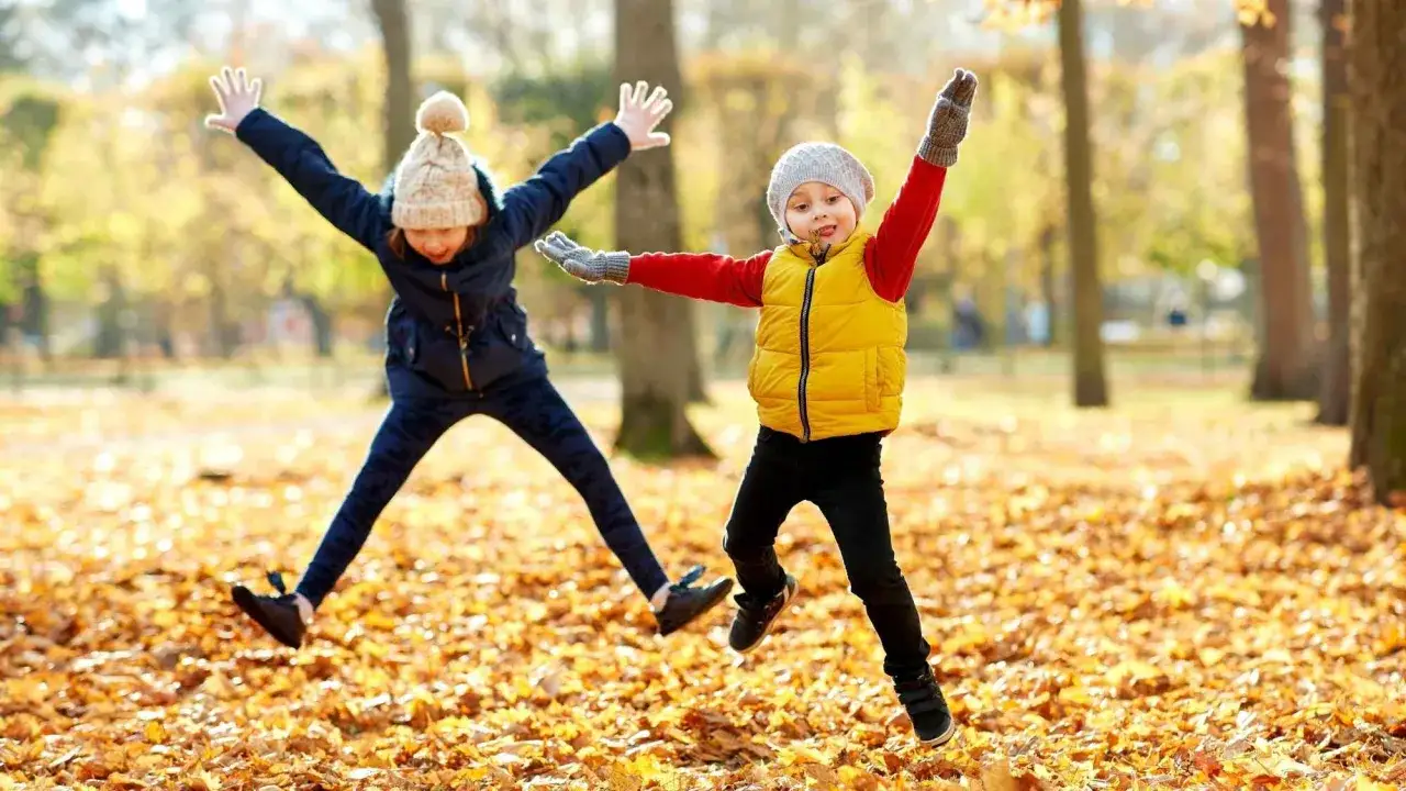Zwei Kinder springen fr&ouml;hlich durch Laub. Perfekt f&uuml;r herbst angebote kita!