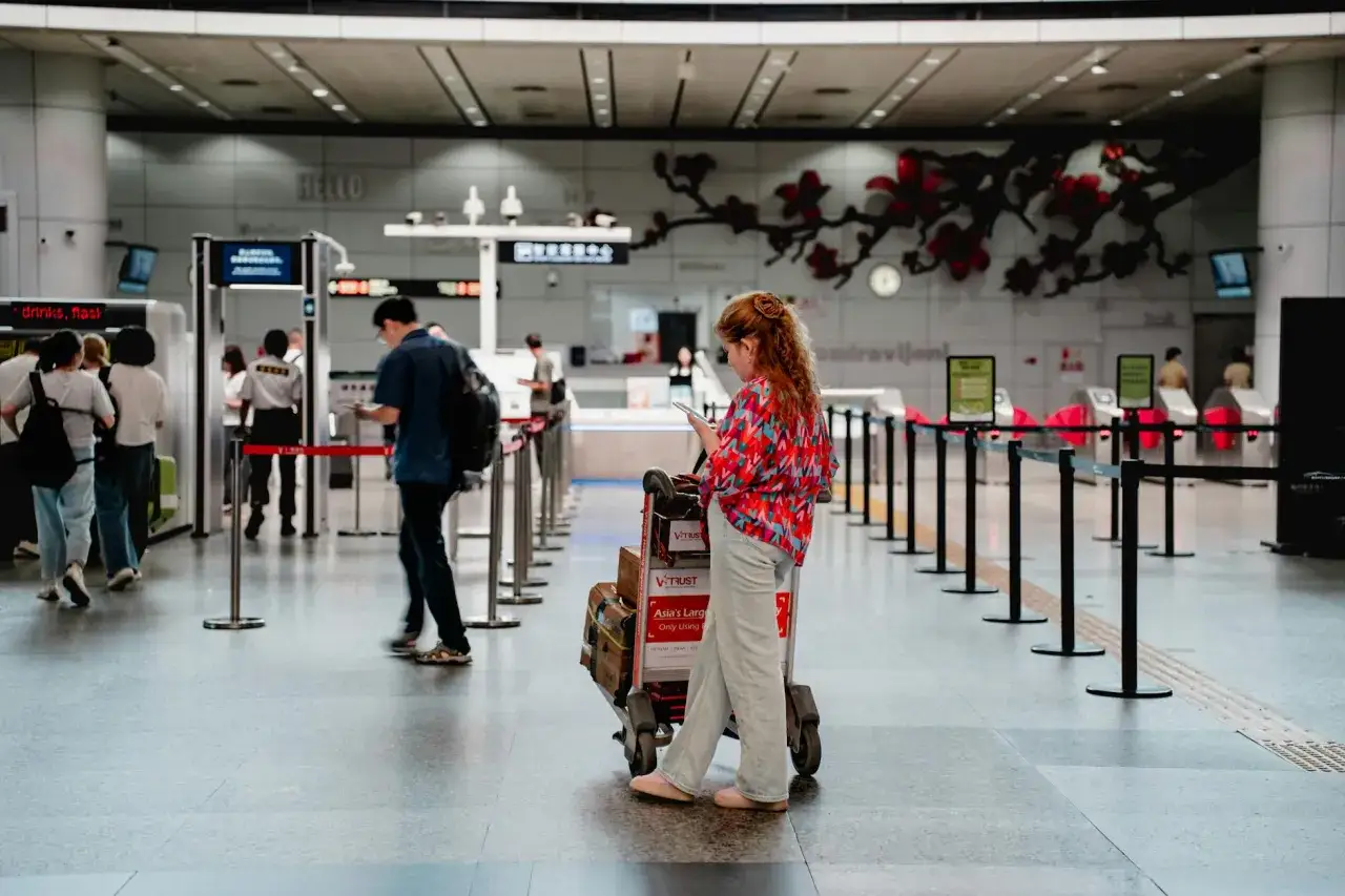 Kobieta z wózkiem bagażowym sprawdza telefon na lotnisku. Czy to będzie lot czarterowy? Czekamy na boarding.