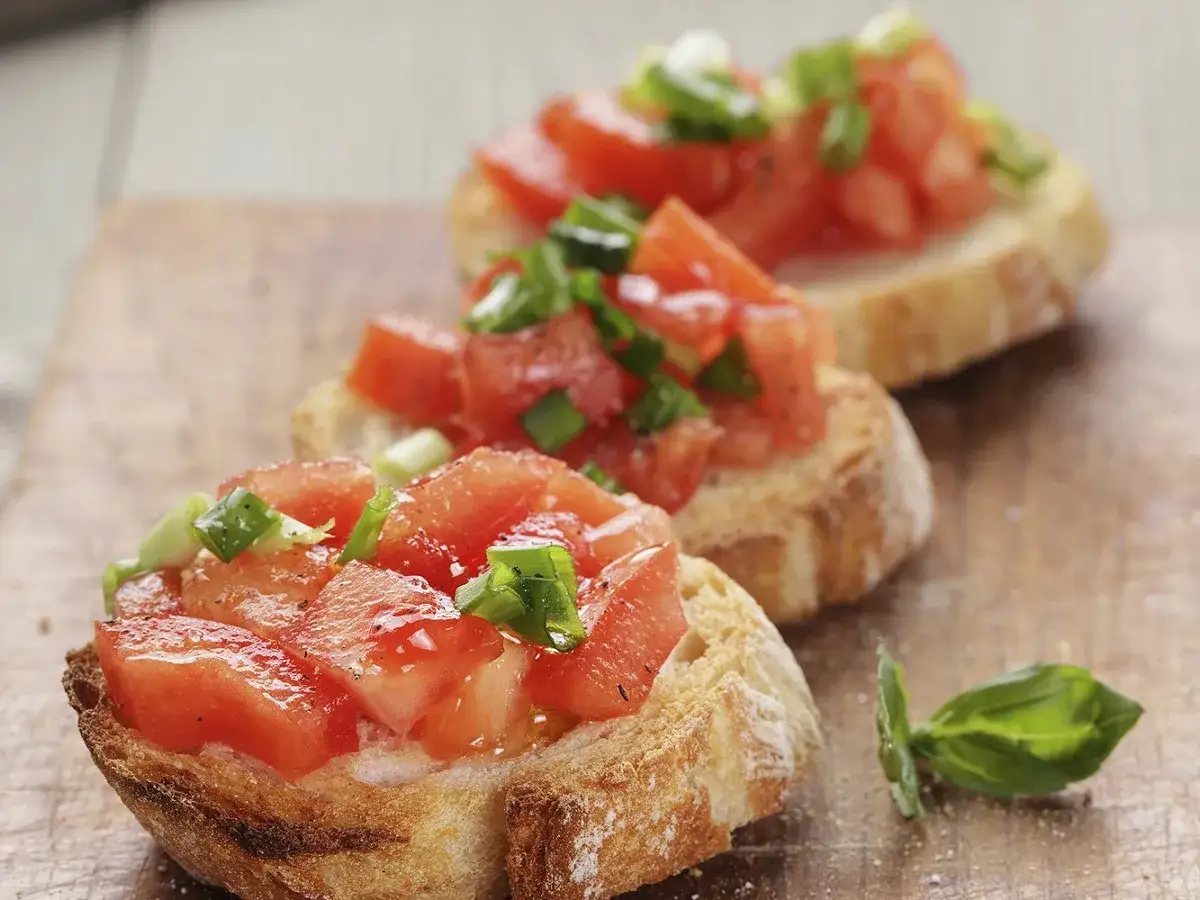 Trois d&eacute;licieuses bruschettas garnies de tomates fra&icirc;ches et d'oignons verts, parfaites pour une recette facile.