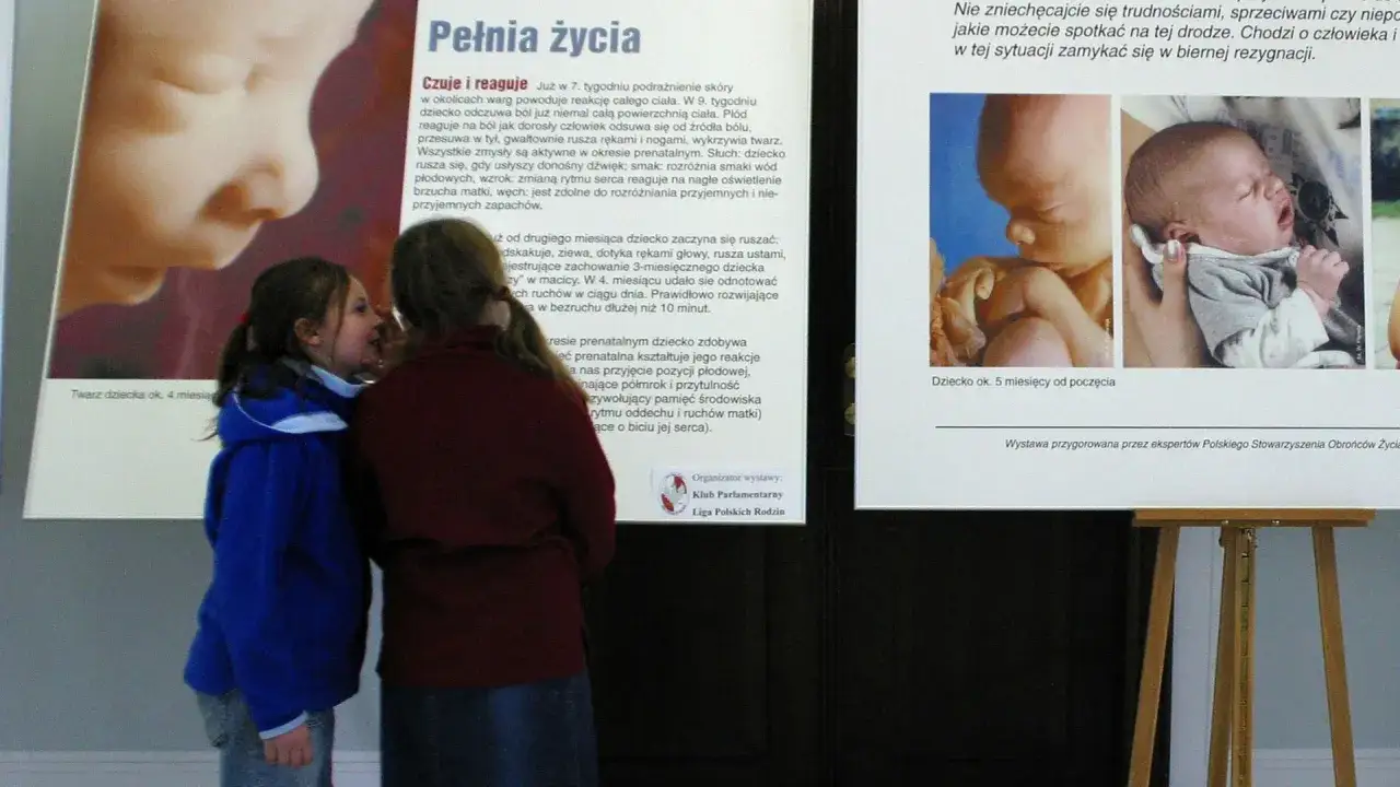 Dwie dziewczynki patrzą na wystawę o rozwoju płodu. Czy antykoncepcja to grzech? Obok zdjęcia płodów i noworodków.
